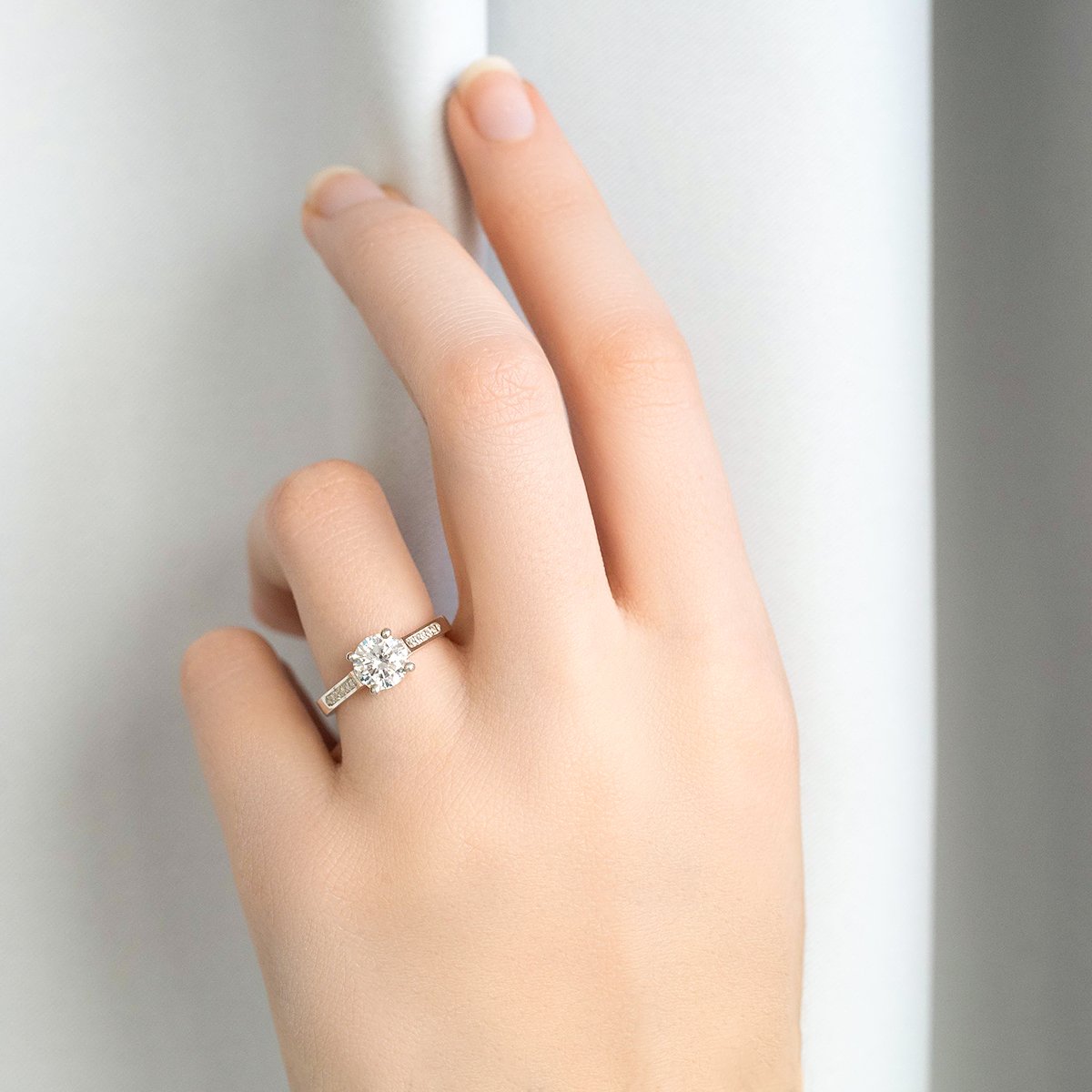 lady wearing round brilliant cut engagement ring with elegant baguette cut diamond shoulders