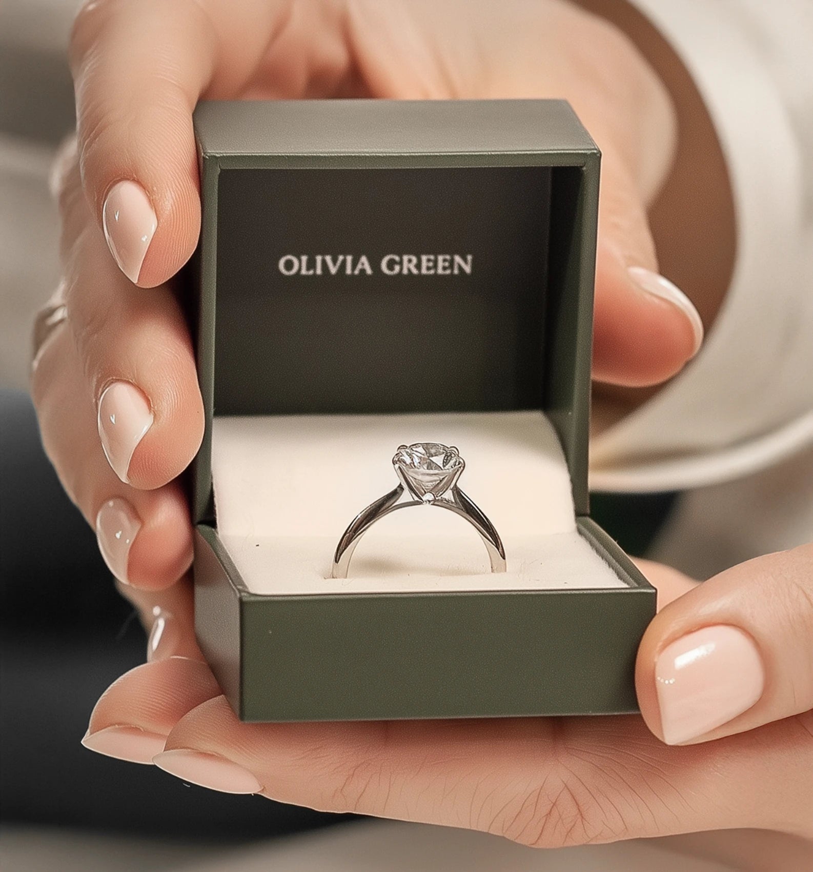 Diamond ring in an open 'Olivia Green' box held by a hand.
